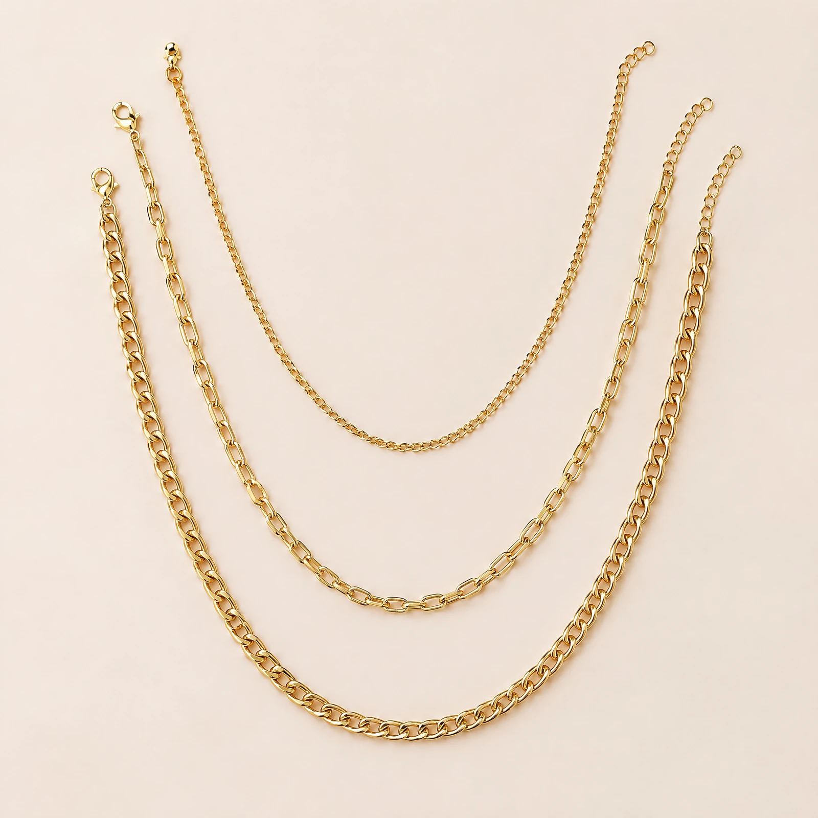 Three plain gold-tone chain necklaces layered in curves on a blush background