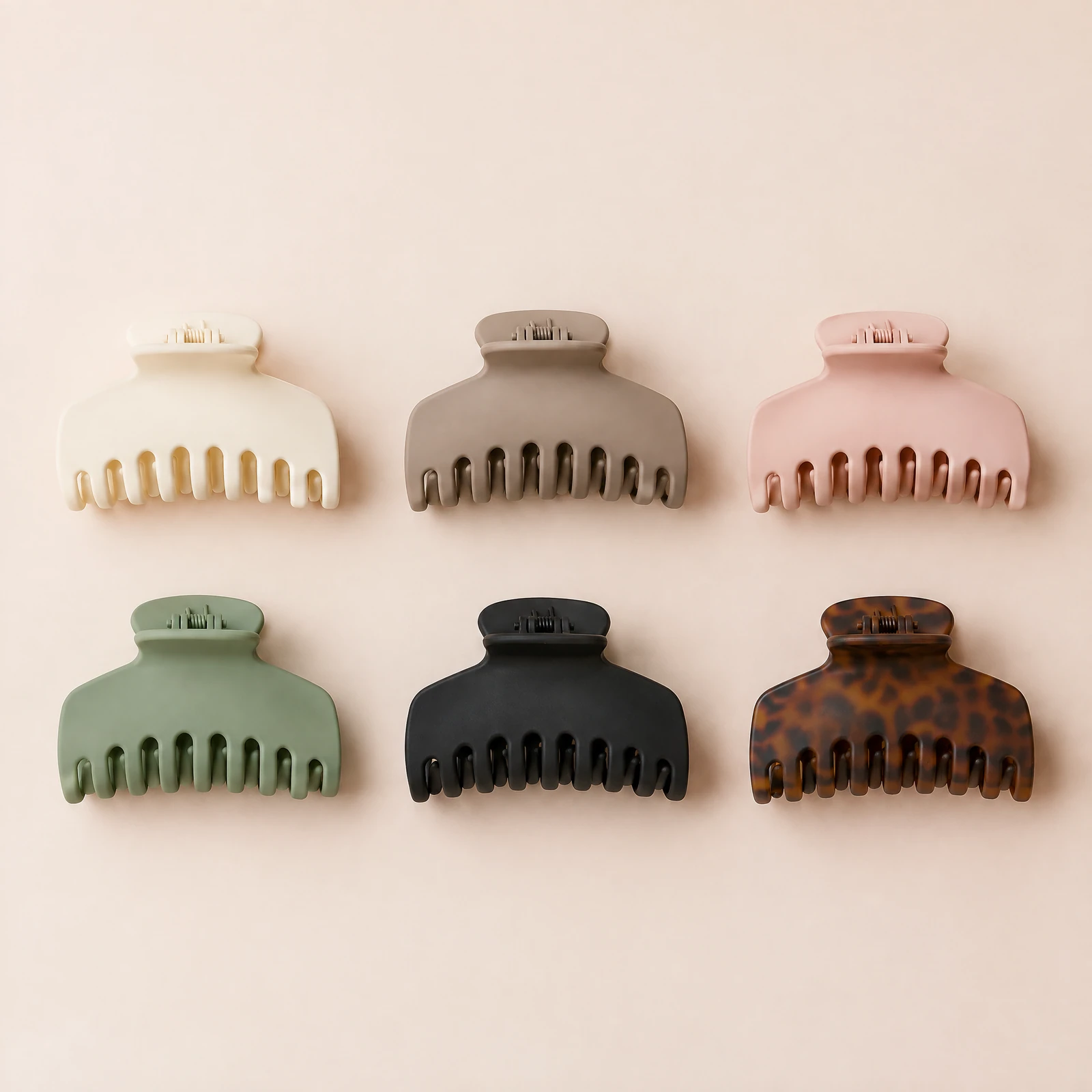 Six claw hair clips in assorted neutral colors arranged in a grid on a blush background