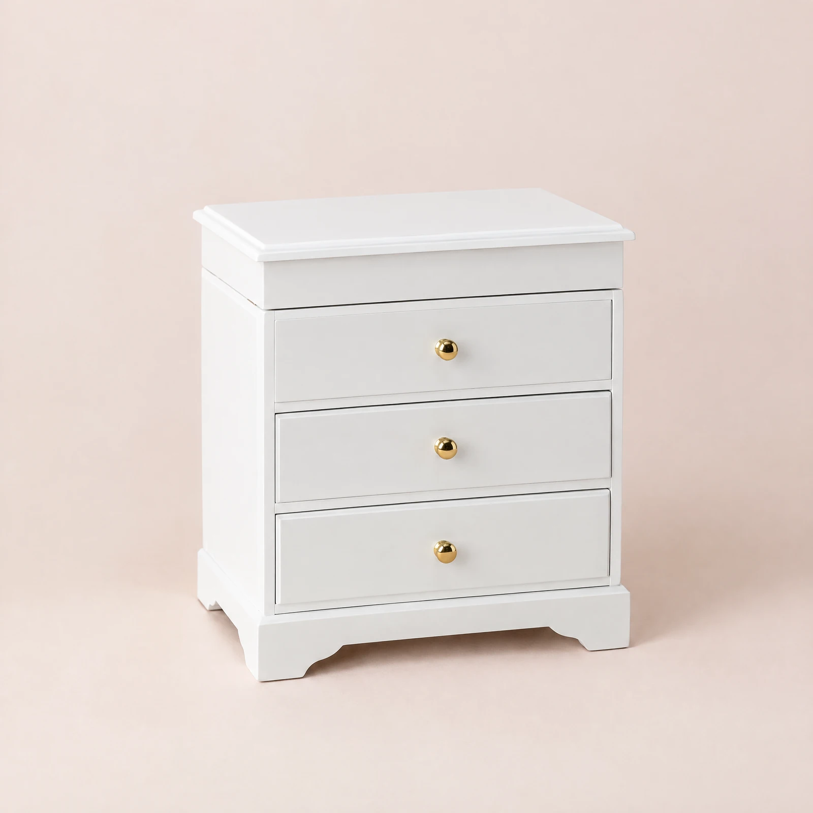 White three-drawer jewelry chest with gold-tone knobs on a blush background